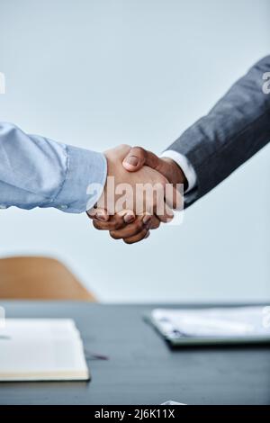 Vertical close up of two business people shaking hands at meeting against simple blue background Stock Photo