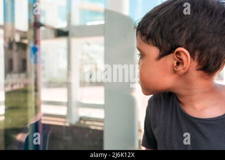 Latino boy pressing his face against glass outdoors. Concept of self discovery . Stock Photo