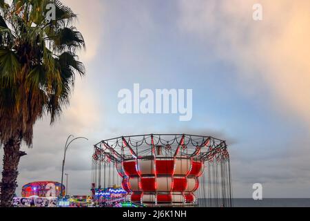 High-section of a chain swing and other rides of the Luna Park on the waterfront against cloudy sky and sea at dusk, Sanremo, Imperia, Liguria, Italy Stock Photo