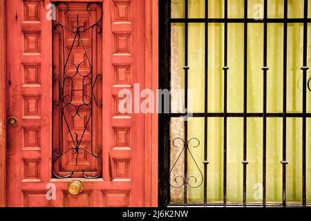 Wooden door next to window with gree curtain and forged metal grill Stock Photo