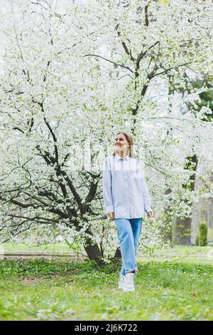A woman in a white shirt and jeans with glasses in her hands in a spring garden. Stock Photo