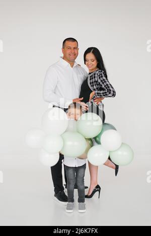 A beautiful happy young family with a son are waiting for a new family member. A pregnant woman with a child and her husband are holding balloons in t Stock Photo