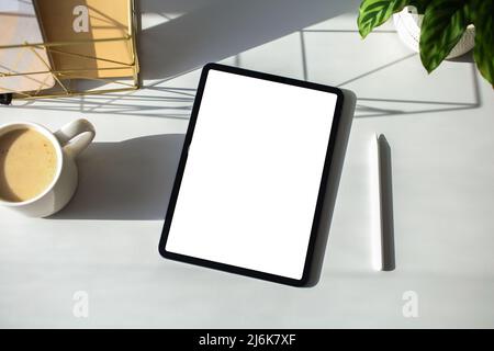 Flat lay blank screen tablet and pen, cup of coffee, paper notebooks, green plant on white table. Aesthetic home office desk, elegant feminine workspa Stock Photo