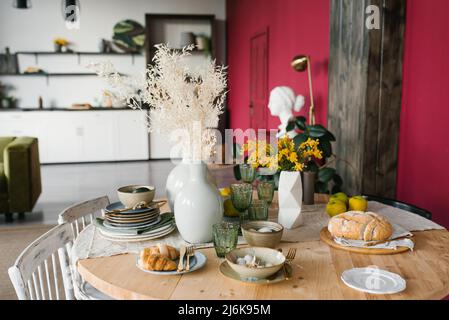 Festive Easter table with mimosa flowers in a vase and traditional food, eggs. The interior of a bright living room with a round set table Stock Photo