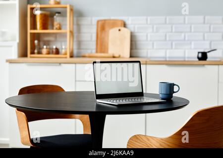 Minimal home workplace with open laptop on black kitchen table with wooden chairs, copy space Stock Photo