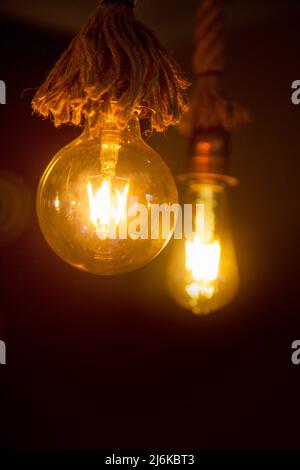 Edison light bulb, vintage hanging Edison light bulb over dark background. Bulbs hanging with old retro rope. isolated on black with copy space, blank Stock Photo