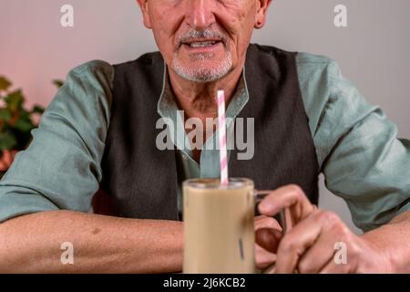 casual dressed mature man sitting at a table drinking iced coffee through a straw Stock Photo