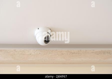 One single round security camera on a ceiling in a bright room, CCTV cam object detail, closeup, nobody. Safety, modern video surveillance system, gua Stock Photo