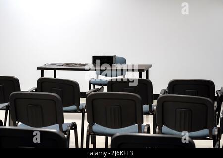 Simple empty prepared lecture hall, conference room chairs and presenter's desk with a video projector, white screen, nobody, no people. Vacant class Stock Photo
