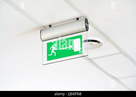 Modern green emergency exit route door arrow sign on the ceiling, object detail, closeup, nobody. Corporate business office building workplace safety, Stock Photo
