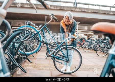 Senior woman gets the bike in a parking Stock Photo