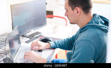 A man in a turquoise sweater in a bright office while working at a computer close-up. Work illustration Stock Photo