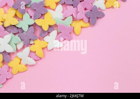 Colorful butterflies, a popular sugar confectionery topping, lie on a pink background diagonally in the left corner. Stock Photo