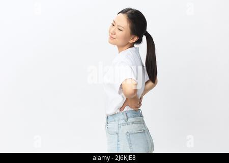 Back pain. Suffering from osteochondrosis after long study pretty young Asian woman touching painful lower back posing isolated on white background Stock Photo