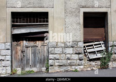 Two old dilapidated cracked wooden boards entrance doors partially covered with broken rusted metal blinds and wooden boards with stacked Stock Photo