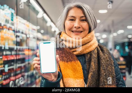 Senior woman at the supermarket shows the screen of her smartphone Stock Photo