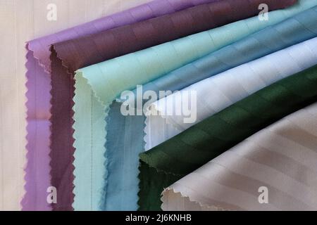 Samples of color stripe satin background. Beautiful high-quality fabric for sewing bed linen. Cotton textiles of white, green, burgundy color top view Stock Photo