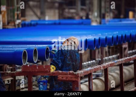 Worker painting new cast iron pipes in blue color. Stock Photo