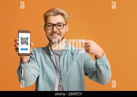 Handsome man pointing at smartphone with QR code on screen against orange background Stock Photo