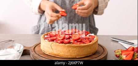 Woman decorating tasty pie with strawberry at table in kitchen Stock Photo