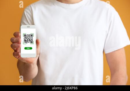 Man holding smartphone with QR code on screen against orange background, closeup Stock Photo