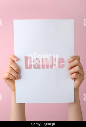 Female hands holding paper with word DANKE (German for Thanks) on pink background Stock Photo
