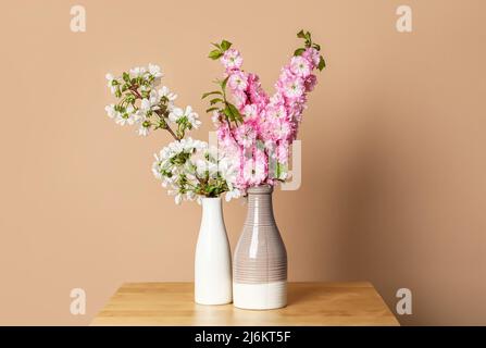 Ceramic vases with beautiful blooming branches on table near beige wall Stock Photo