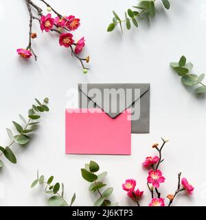 Red plum flowers on twigs, fresh eucalyptus leaves. Blank pink card with grey envelope. Stock Photo
