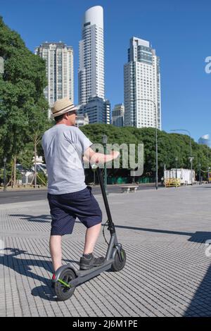 Latin senior man riding his electric kick scooter around the city in summer. Concepts of sustainability, summer tourism, active life, clean energy and Stock Photo