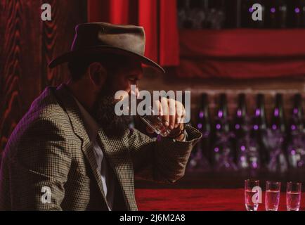 Handsome bearded man enjoying whiskey in bar. Hipster drinking in bar. Brutal guy drinking alcohol. Stock Photo