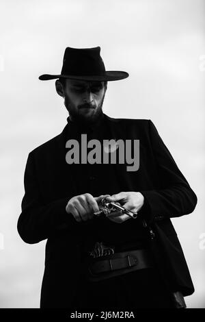 Cowboy shooter in black suit and cowboy hat. Serious man with wild west guns, retro pistol revolver and marshal ammunition. American western Sheriff Stock Photo