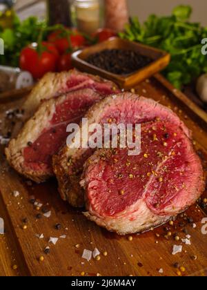 Macro shot. Juicy raw steaks breaded in fragrant seasonings on a wooden cutting board. In the background are tomatoes, garlic, peppers. The concept is Stock Photo