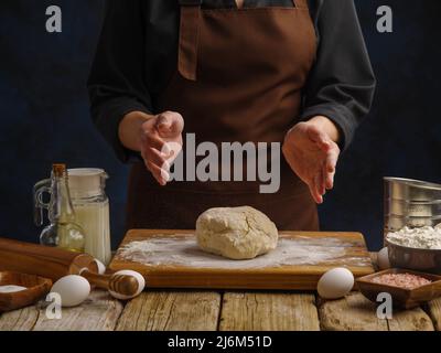 On a wooden cutting board, dough prepared by the hands of a professional chef. The concept is the preparation of products from dough - pasta, pizza, b Stock Photo