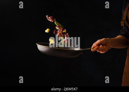 Sea food. Octopuses with lemon slices and vegetables in a pan in frozen flight on a black background. Recipes for restaurant and home cooking, healthy Stock Photo