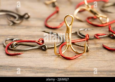Close up of fishing hooks of different shapes and sizes scattered on a wooden table. Emphasis on golden triple hook in the foreground. Stock Photo