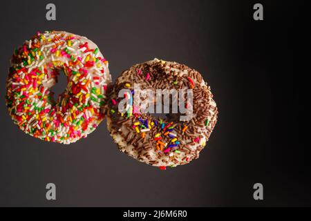 Two multi-colored sweet donuts on a gray background in a frozen flight. Sweet food, calories, fast food, happiness hormone. Holiday, birthday invitati Stock Photo