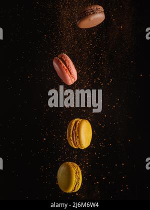 Yellow and pink macaroons with a flow of chocolate chips in a frozen flight on a black background. Birthday, holiday, sweets, confectionery, shop. The Stock Photo