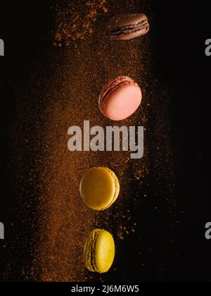 Macaroons - French pastries in a frozen flight and a stream of chocolate chips on a black background. Festive composition. Birthday, sweet food. Adver Stock Photo