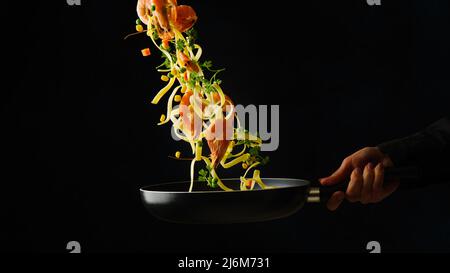 Appetizing Italian pasta with king prawns and vegetables in frozen flight on a black background. Healthy vegetarian gourmet food, healthy lifestyle. R Stock Photo