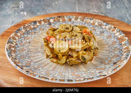 Pieces of zucchini with tomatoes on plate on wooden background Stock Photo