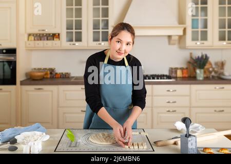 Young middle Asian woman is cooking baking in the interior of a modern home kitchen. Stock Photo