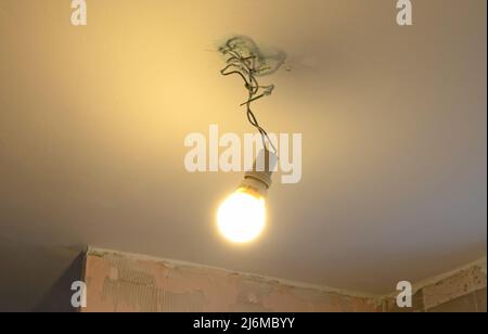 Lightbulb hanging temporarily on a ceiling, bringing light in the darkness Stock Photo