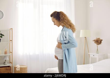 Young pregnant woman who gently looks and touches her belly listening to movements of baby in womb. Stock Photo