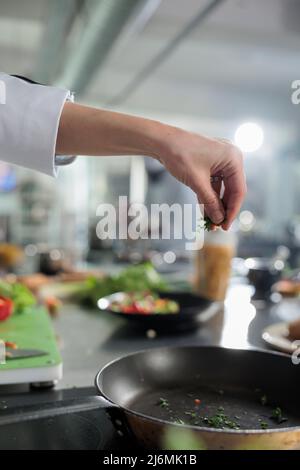 Close up of gastronomy expert hands garnishing gourmet dish with chopped fresh herbs in restaurant kitchen. Head chef cooking food for dinner service while adding ingredients to meal. Stock Photo