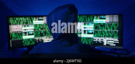 Rear view od hooded hacker by computer in the dark room at night, cyberwar concept. Stock Photo