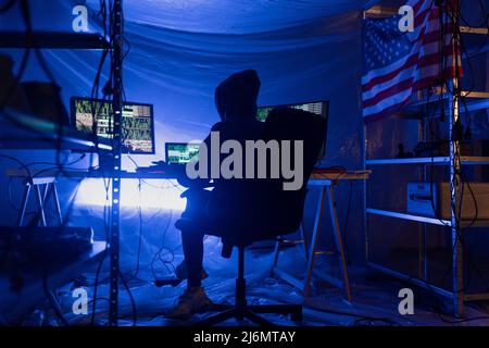 Rear view od hooded hacker by computer in the dark room at night, cyberwar concept. Stock Photo