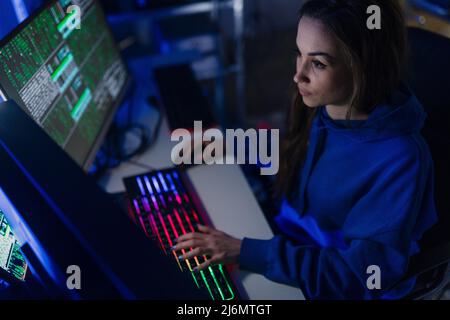 Young woman hacker by computer in the dark room at night, cyberwar concept. Stock Photo