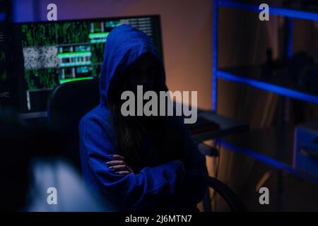 Hooded anonymous hacker by computer in the dark room at night, cyberwar concept. Stock Photo