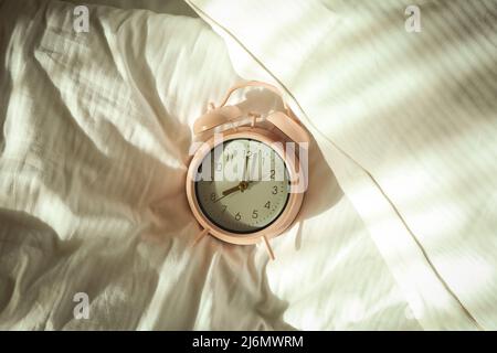Pink alarm clock on the bed in the morning Stock Photo