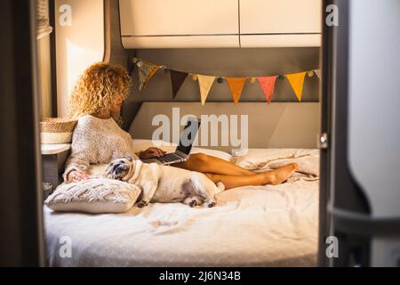 Attractive woman have relax inside van camper laying on bed and using laptop computer connection. Adorable dog sleeping near her. Female independent